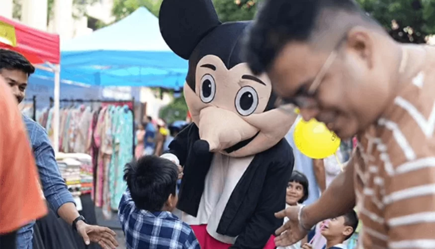 Child high-fiving a person in a Mickey Mouse costume at a community event in Downtown Powai