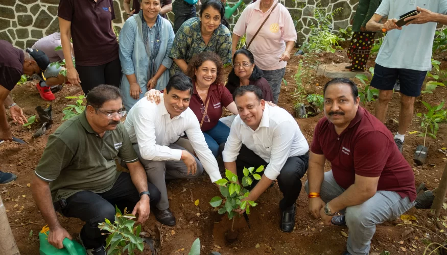 Group of people participating in a tree planting event at Downtown Powai, smiling and posing around a newly planted sapling